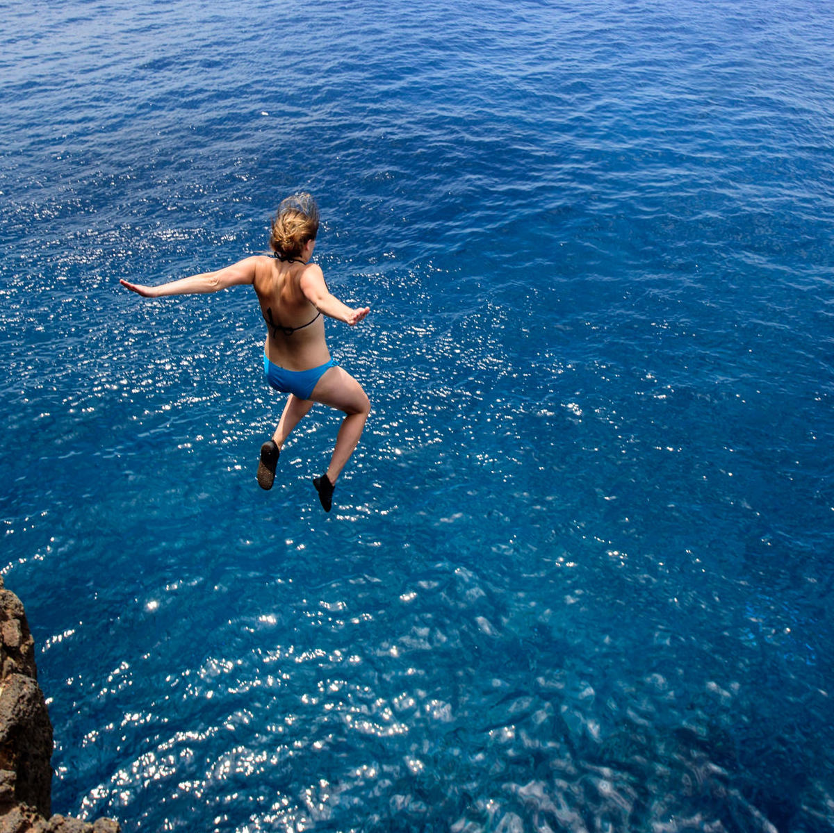 woman jumping off a cliff into the Pacific Ocean