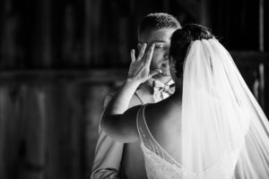 Black and white photo of bride wiping groom's tears during first look