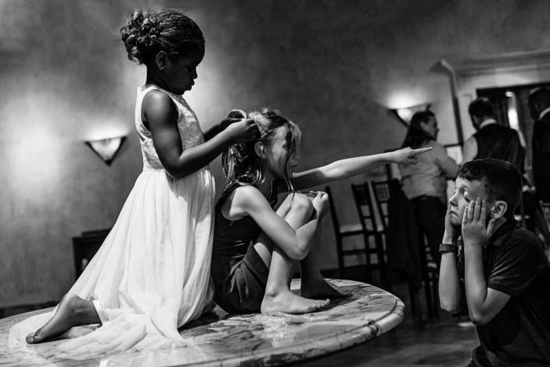 kids on a table at a wedding with a girl bossing an exhausted boy around