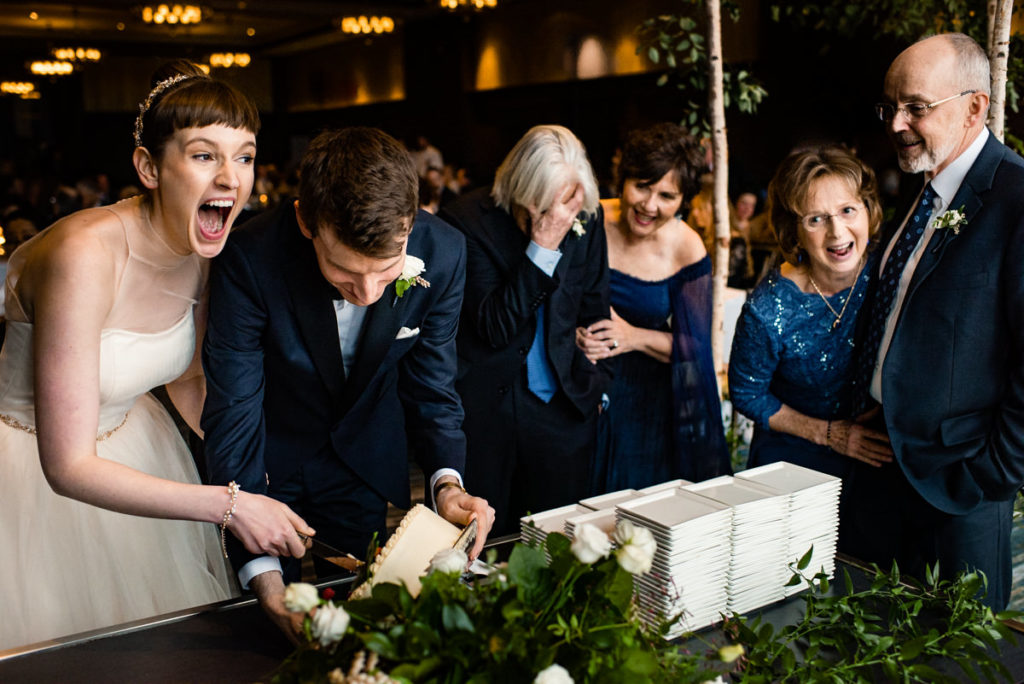 the couple and their parents all laugh and cringe after the bride and groom spill the cake during its cutting