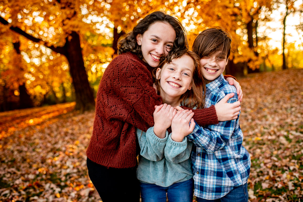 Three siblings hug for a family portrait in front of fall colors