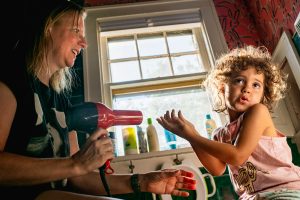 Mom blow dries her daughter's newly painted fingernails in their bathroom