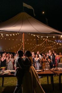 Wedding couple begins to kiss after a cake cutting and their friends and family cheer in the background