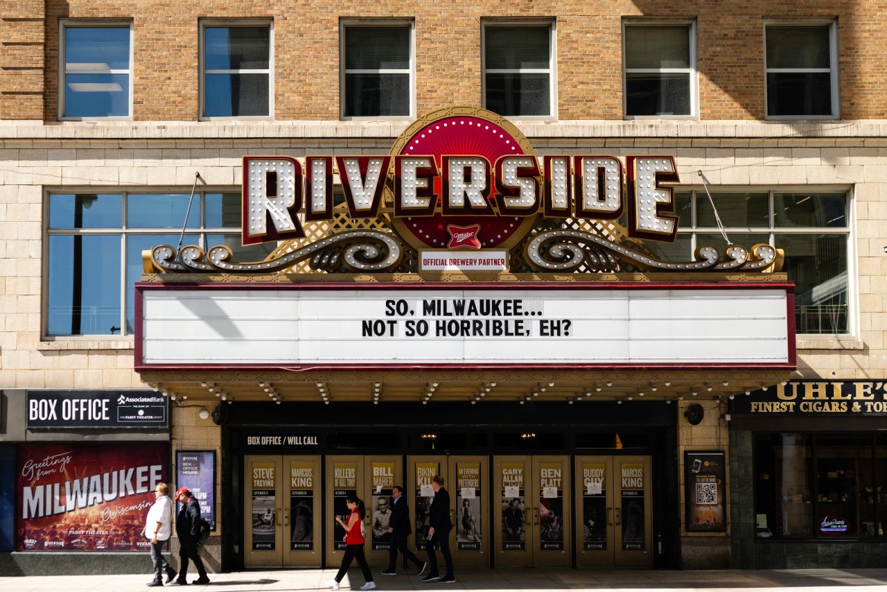 The Riverside Theater marquee in downtown Milwaukee displays the message “So, Milwaukee… Not so horrible, eh?” during the 2024 Republican National Convention, as people walk by the box office and show posters.