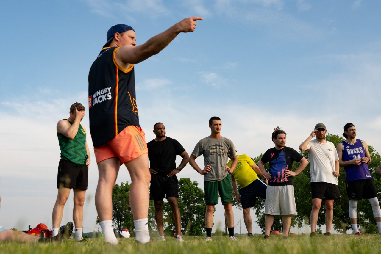 A Wisconsin Wombats coach gestures while giving instructions to players standing in a row during Australian rules football practice at Olbrich Park in Madison.